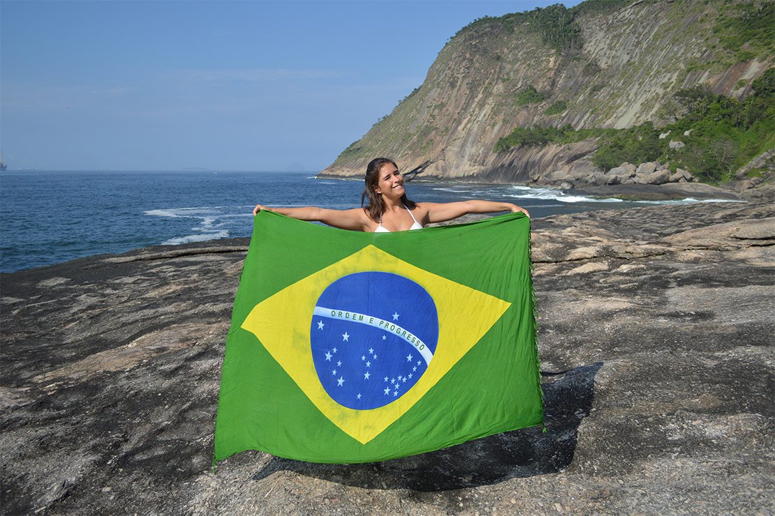 Alezzia segurando a bandeira do Brasil em frente ao mar