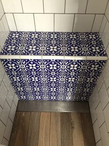 ralo linear inox sobre piso de madeira no banheiro e ladrinho florido azul